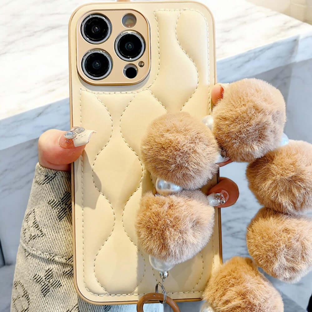 a person holding a phone case with four pom poms