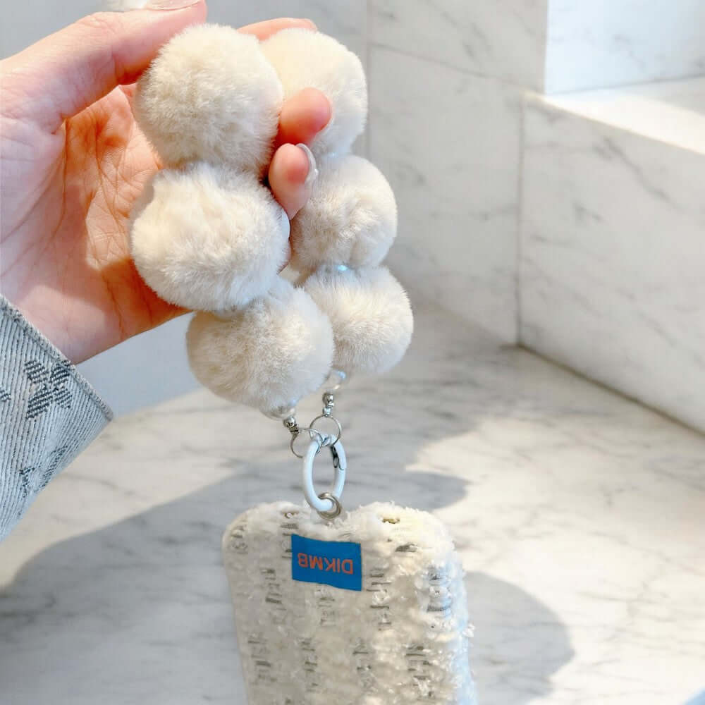 a hand holding a white pom pom keychain